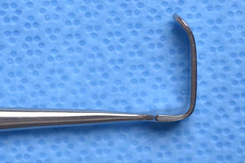 This double-ended retractor has one end that is angled and blunt.  The other end, which is directed in the opposite direction, is rake shaped with three prongs which can be either sharp or blunt. This retractor has many uses and one such example is for elevating malar tissues during a mid-face lift
