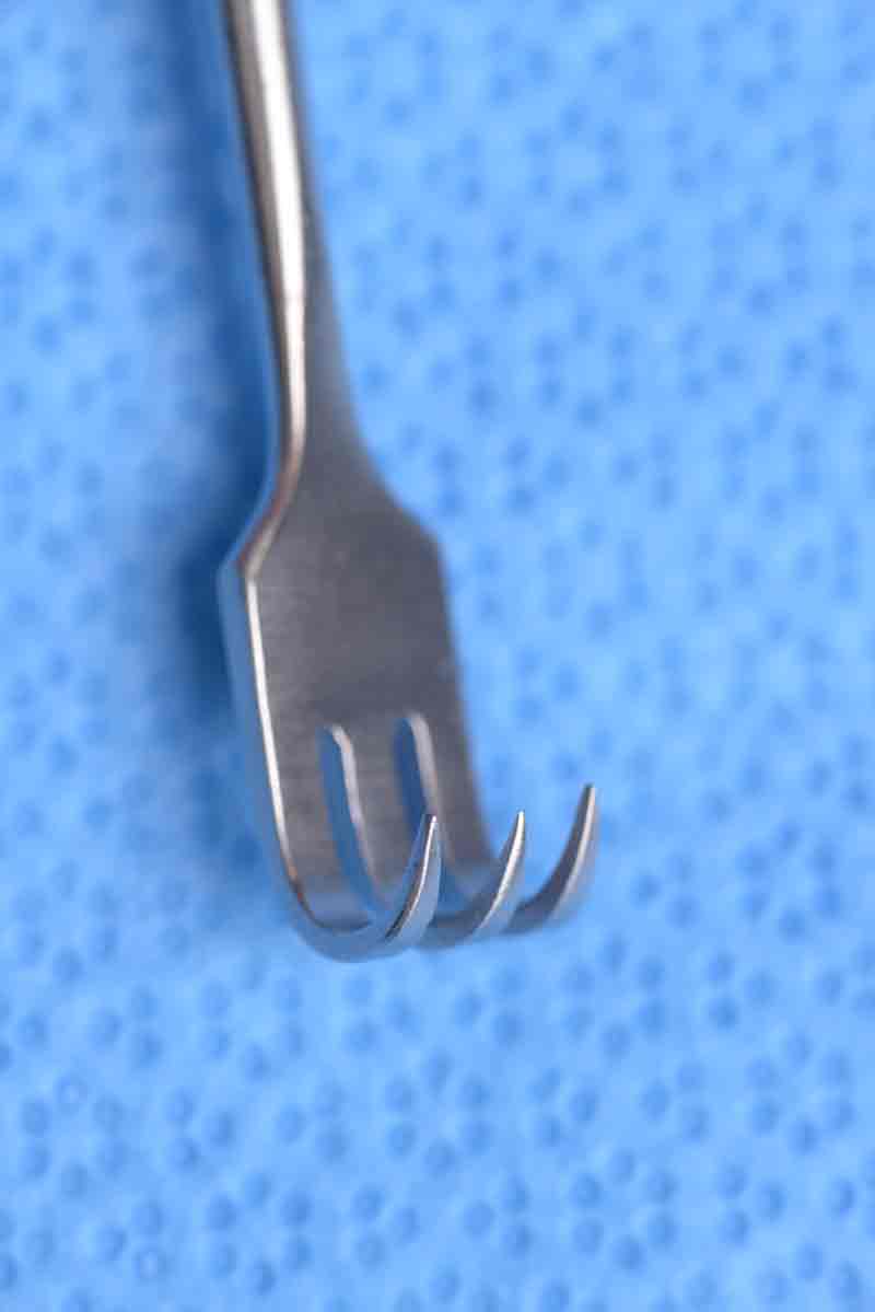 This double-ended retractor has one end that is angled and blunt.  The other end, which is directed in the opposite direction, is rake shaped with three prongs which can be either sharp or blunt. This retractor has many uses and one such example is for elevating malar tissues during a mid-face lift